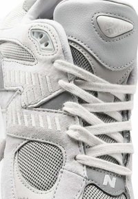 Sneakers grigi con dettagli in suede, mesh e gomma. Le caratteristiche includono fori per i lacci, collo imbottito e lacci piatti. Variazione di texture sottile in tutto il modello.