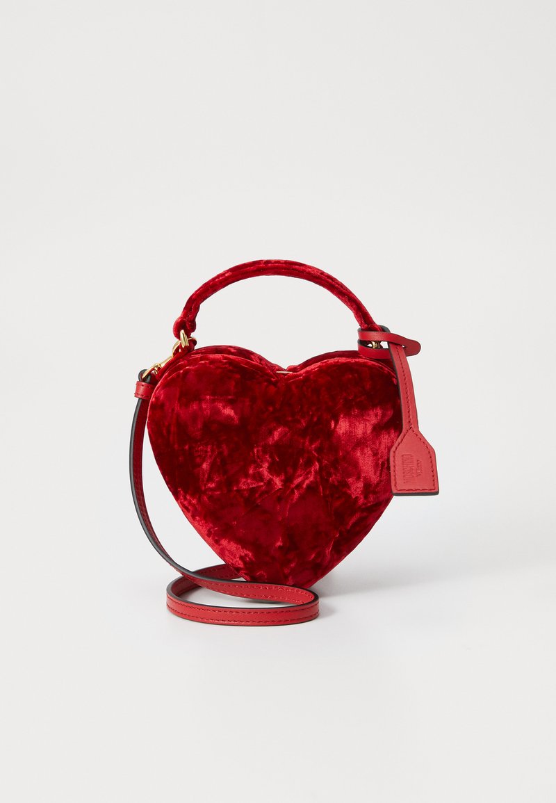Sac en velours rouge en forme de cœur avec une courte anse et une bandoulière amovible. Doté de quincaillerie dorée et d'une étiquette en cuir.