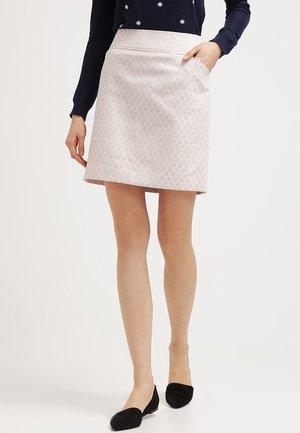 Femme portant une jupe trapèze rose pâle à motifs avec poche, un pull bleu marine avec des détails d'étoiles blanches, et des ballerines noires, debout sur un fond blanc.