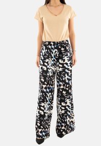 Maglietta beige a scollo a V abbinata a pantaloni a palazzo con motivo in bianco e nero, caratterizzati da dettagli blu e una comoda cintura elastica.