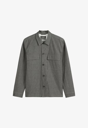 Chemise grise à manches longues avec un col classique, deux poches avant et fermeture à boutons, fabriquée en tissu doux avec un aspect texturé.