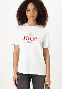 Balta medvilninė marškinėlių su apvalia iškirpte, trumpomis rankovėmis ir ryškiu raudonu bei mėlynu "JOOP! JEANS" logotipu su apvaliu simboliu viršuje.