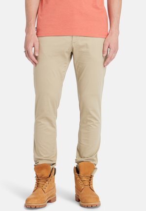 Pantalons beiges à coupe slim, associés à des bottes marron à lacets avec un col rembourré et une semelle en caoutchouc texturée.