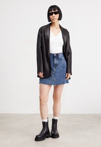 Svart skinnblazer, hvit v-hals topp, blå denim mini-skjørt med råkant, svarte chunky støvler, og mørke solbriller. Enkelt, dristig design.