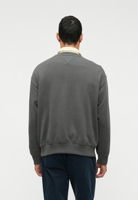 Γκρίζα φούτερ μπλούζα με στρογγυλή λαιμόκοψη, ριμπ μανίκια και στρίφωμα, με λεία υφή και χαλαρή εφαρμογή, σε συνδυασμό με σκούρους παντελόνες.