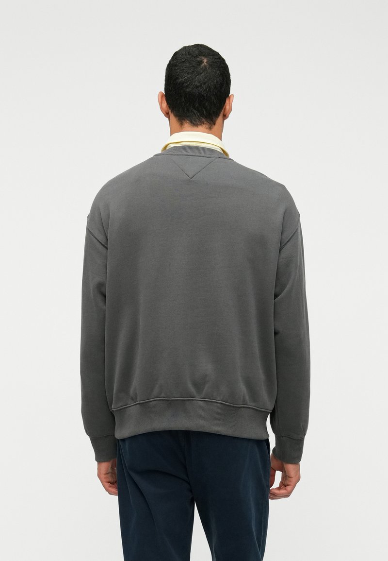 Gray sweatshirt with a crew neckline, ribbed cuffs and hem, featuring a subtle texture and a relaxed fit, paired with dark trousers.
