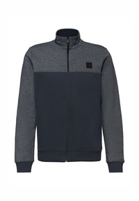 Veste zippée pour hommes avec partie supérieure et manches gris foncé et corps inférieur bleu marine, dotée d'un col montant et d'un petit écusson sur la poitrine.