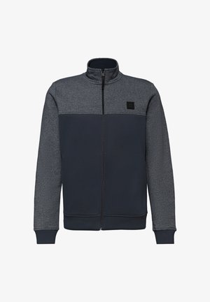Męska kurtka na zamek błyskawiczny z ciemnoszarym górnym partem i rękawami oraz granatowym dolnym partem, z wysokim kołnierzem i małą naszywką na piersi.