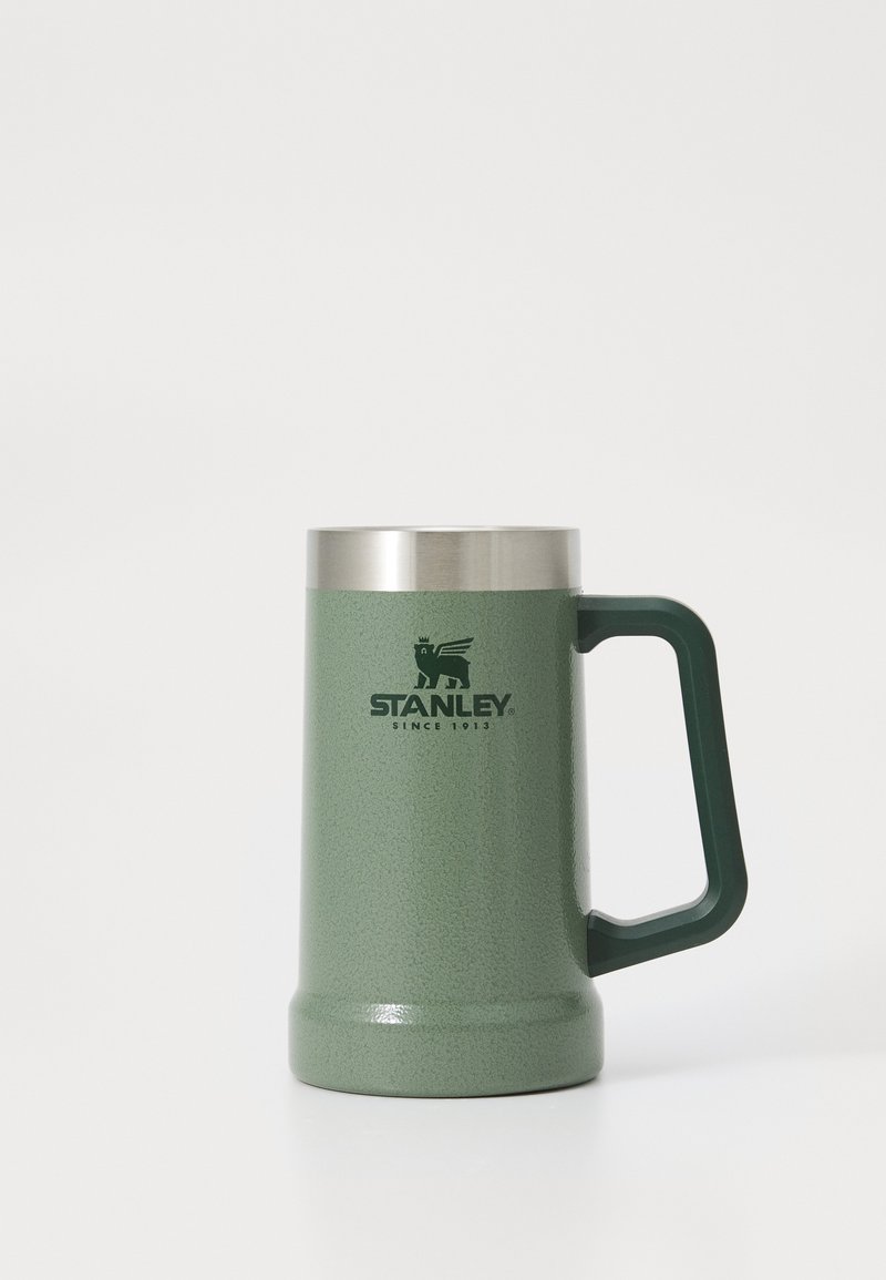 Caneca metálica verde com um acabamento texturizado, borda em aço inoxidável e uma pega robusta; apresenta o logótipo em relevo "STANLEY" na frente.