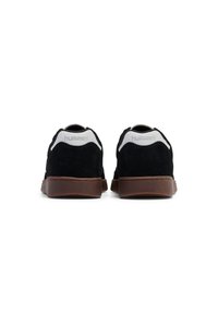 Schwarze Wildleder-Sneaker mit brauner Gummisohle, weißem Fersenkontrast und geprägtem Branding auf der Ferse. Klassisches Low-Top-Design.
