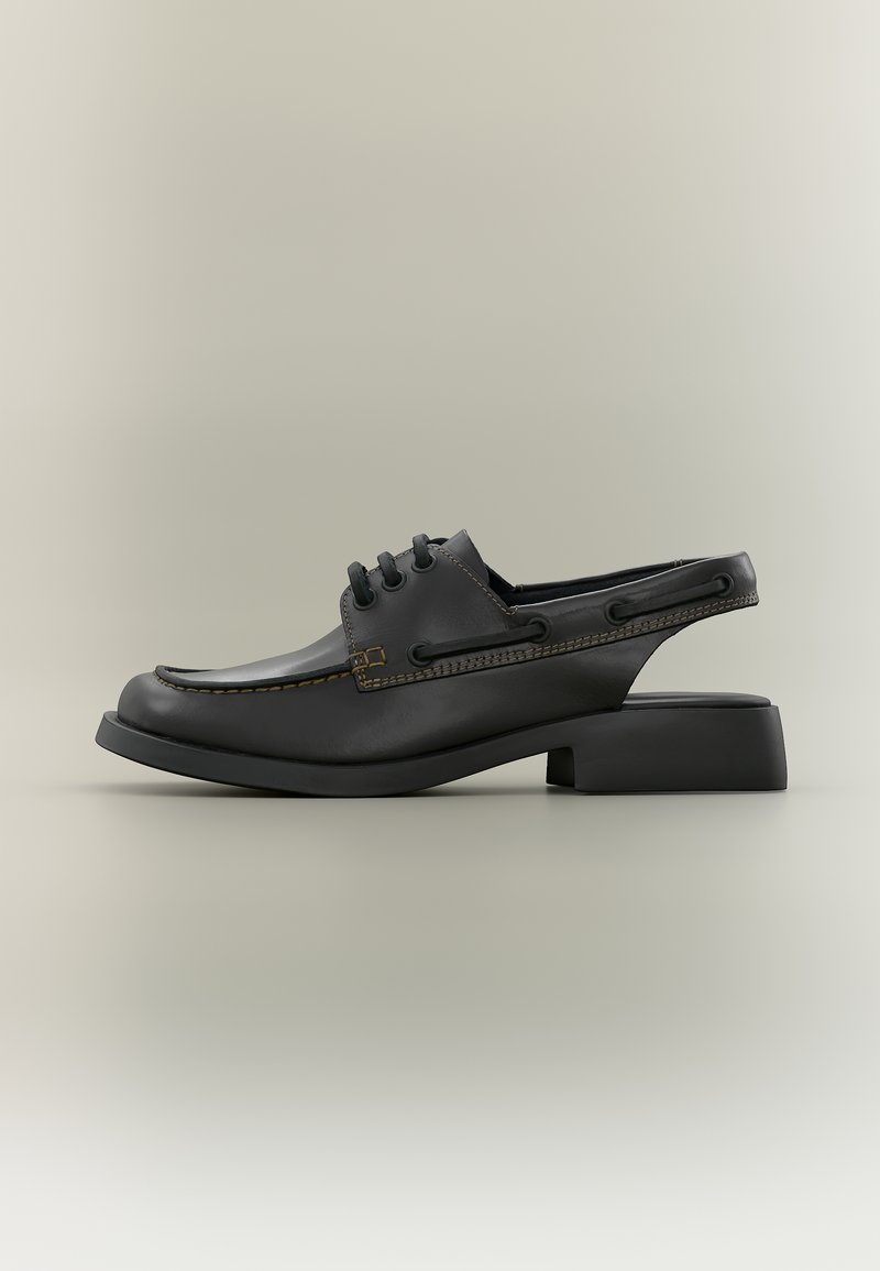 Chaussure hybride en cuir noir avec lacets à l'avant, bride arrière ouverte, bout carré et petit talon bloc, sur fond beige uni.