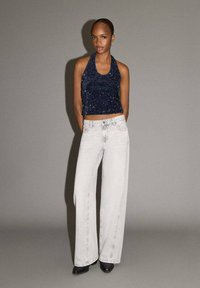 Námornícky trblietavý top na šnurovanie zladený so svetlošedými širokými džínami a čiernymi špicatými členkovými čižmami. Hladké textúry a voľný strih oboch kusov.