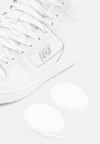 Hvite høye sneakers i teksturert lær, flate lisser og en grå logo-lapp. To ekstra hvite runde lisser plassert ved siden av skoen.