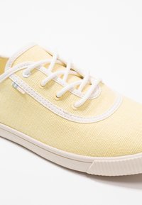 Baskets en toile jaunes avec lacets blancs, tige texturée, bout rond et semelle en caoutchouc léger. Présente des accents subtils en bleu et beige.