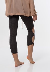 Leggings noirs avec détails découpés sur les côtés, coupe ajustée et longueur trois-quarts. Portés avec un top ample en maille brun clair.