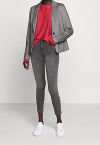 Szary żakiet, czerwona koszula, szare rurki i białe trampki. Żakiet ma klapy w stylu oszlifowanym, dwie przednie kieszenie i teksturowany materiał.