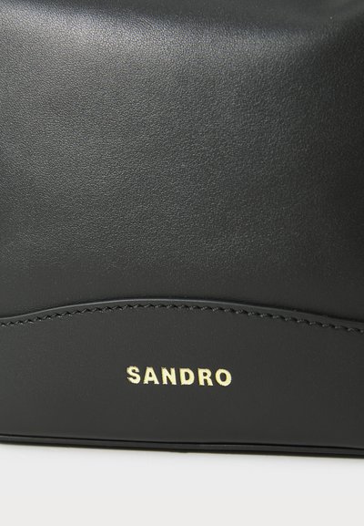 Crni kožni dodatak s glatkom teksturom, zakrivljenim šavom i zlatno otisnutim logom "SANDRO".