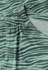 Tessuto verde con strisce zebra nere, con bande elastiche arricciate nella parte superiore. Texture liscia con una leggera lucentezza.