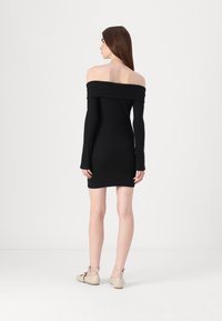 Vestido preto de malha canelada, aos ombros, com mangas longas, ajuste justo ao corpo e barra reta, combinado com sapatos de tira no tornozelo em bege.