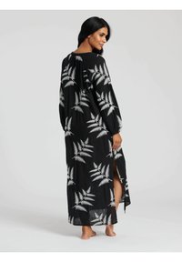 Czarna maxi sukienka o luźnym kroju, z białymi wzorami paproci, długimi rękawami i bocznymi rozcięciami dla swobody ruchów.