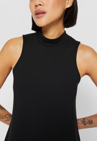 Svart ärmlös topp med hög halsringning, tillverkad av slät tyg. Har en figurnära design som framhäver axlarna och halsringningen.