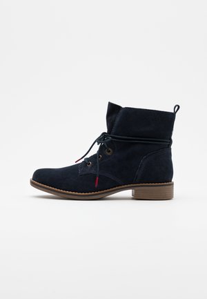 Granatowy zamszowy botek za kostkę z zaokrąglonym noskiem, sznurowanym przodem, pętelką do ściągania na pięcie oraz niskim, drewnianym obcasem warstwowym.