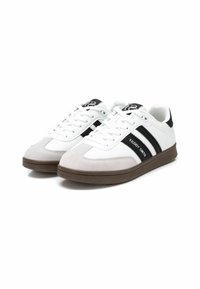 Sneaker bianche con accenti neri e grigi, dotate di una punta in suede, corpo in pelle liscia e suola in gomma marrone. Nome del marchio "Teddy Smith" visibile.