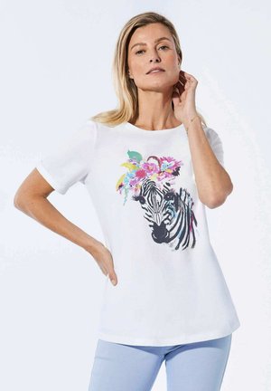 T-shirt blanc avec un graphique de zèbre orné de fleurs colorées. Manches courtes, col rond, texture lisse. Pantalons bleu clair.