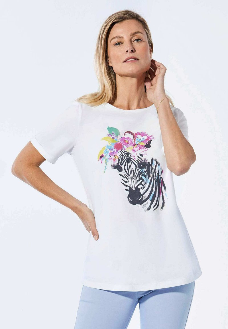 Witte T-shirt met een zebraafbeelding versierd met kleurrijke bloemen. Korte mouwen, ronde halslijn, gladde textuur. Lichtblauwe broek.