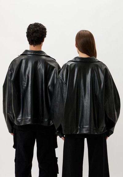 Black faux leather jackets with a boxy silhouette, wide sleeves, and a large collar. Smooth texture, paired with black trousers.