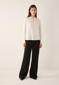 White long-sleeve blouse with a keyhole neck detail, paired with black wide-leg trousers. Smooth fabric and subtle texture in pants.