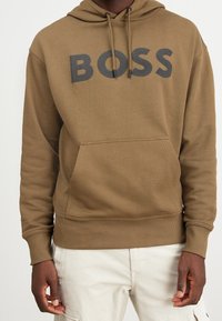 Felpa con cappuccio marrone in misto cotone, con grande logo nero "BOSS", cappuccio con coulisse e tasca frontale a marsupio. Polsini e bordo a coste.