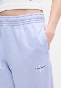 Heledad lavendlised pingul valmistatud spordipüksid, küljeTaskud ja valge brodeeritud "Calvin Klein" logo vasakul reitel. Sile tekstuur.