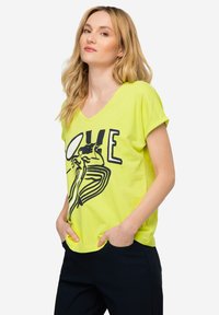 Camiseta verde lima de cuello en v con mangas cortas, que presenta un diseño gráfico en negro y el texto "LOVE" en la parte frontal; tela suave, corte relajado.