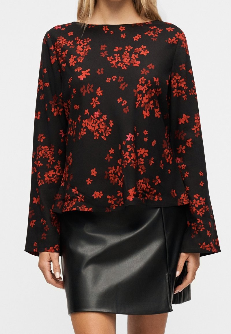 Femme portant un haut noir à manches longues avec un imprimé floral rouge associé à une mini-jupe en cuir noire.