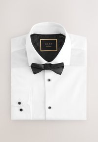 White dress shirt with black buttons and bow tie, folded neatly, showing black polka-dot inner collar label reading "NEXT Occasion."