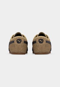 Ζευγάρι χαμηλά παπούτσια με καφέ και μαύρο πουά μοτίβο, μαύρο λογότυπο Puma στη φτέρνα και καφέ σόλες, εμφανιζόμενα από πίσω σε λευκό φόντο.