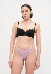 Soutien-gorge en dentelle noire avec armatures et motif floral, accompagné d'un string en dentelle lilas avec des bretelles croisées et un détail en anneau doré.