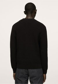 Zwart gebreide trui met een geribbelde textuur, ronde halslijn en lange mouwen. De achterkant heeft iets verlaagde schoudernaden.