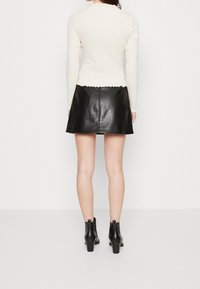 Krämfärgad långärmad topp med scalloperad nederkant, kombinerad med en svart läder minikjol. Svarta klackiga ankelskor fulländar outfiten.