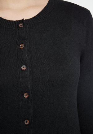 Černý žebrovaný cardigan s kulatým výstřihem a sedmi hnědými knoflíky vpředu. Materiál vypadá měkký a těsně padnoucí.