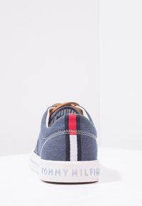 Blå canvas-sneaker med bruna läderdetaljer, vit gummisula och röd- och vitrandig detaljer på baksidan. Varumärkeslogotyp på hälen.