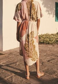 Blumenmuster, knielanges Kleid aus weichem Stoff mit rosa, grünen und braunen Blättern. Getragen mit flachen, silbernen Sandalen auf einem Steinpflaster.