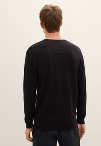 Zwarte gebreide trui met lange mouwen, ronde hals en een rechthoekige accent op de bovenrug. Glad textuur met een aansluitend ontwerp.