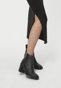 Czarne skórzane botki sięgające kostki ze spiczastym noskiem, teksturowanym wykończeniem, wysokością obcasa około 7 cm i eleganckim designem bez zdobień.