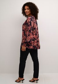 Blouse florale avec un design rose et marine, manches longues, coupe décontractée, associée à un jean skinny noir et des sandales à talons noires.