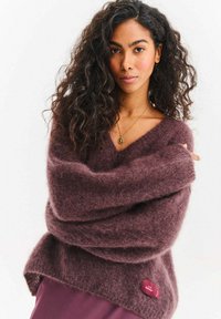 Sweter z dekoltem w serek w dużym rozmiarze w bogatym odcieniu fioletu, wykonany z puszystej mieszanki moheru. Posiada metkę marki na dolnej prawej stronie.