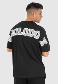 Schwarzes oversized T-Shirt mit weißem Blockschriftzug auf dem Rücken, der "SMILODO" liest. Kurze Ärmel, runder Halsausschnitt und weicher Baumwollstoff.