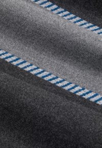 Szara wełniana kołdra o gładkiej fakturze, z niebiesko-białym paskowym wzorem wzdłuż krawędzi. Miękka, ciepła i ułożona w fałdy.