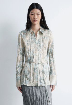 Light beige, pleated shirt with blue floral patterns, button-down front, collared neck, and long sleeves. Includes a tied belt at the waist.